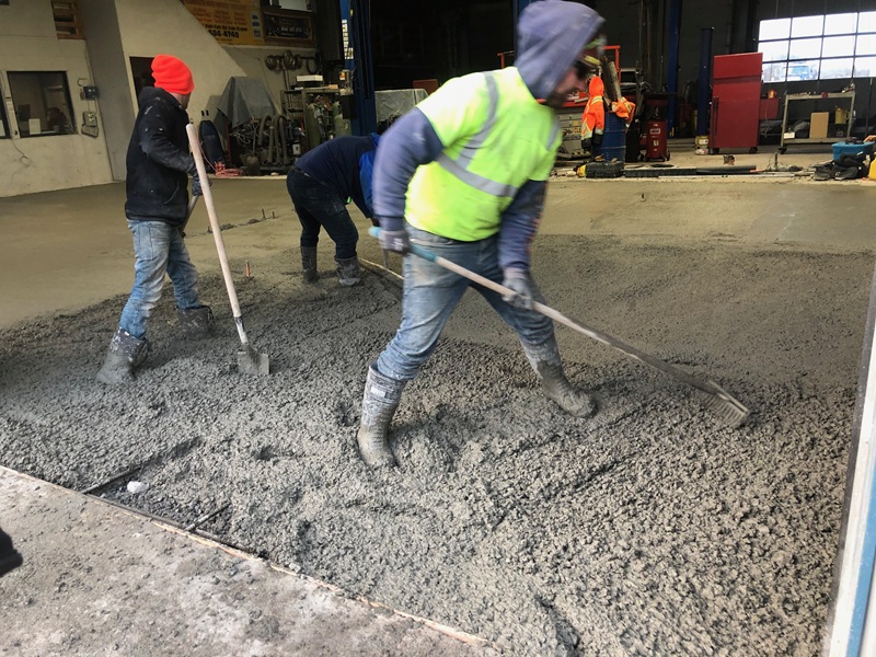 Concrete crew placing and levelling wet concrete on an industrial floor